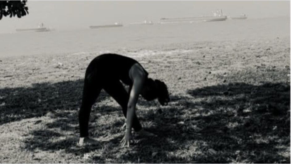 Karuna Grover in a standing forward fold on the grass, seaside